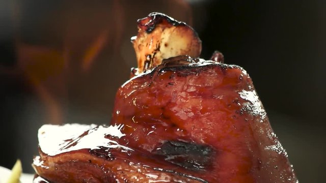 Appetizing lamb shank oiling and burining. Close up macro of roasted shank of lamb burning, slow-mo. Cooking meat at restaurant.