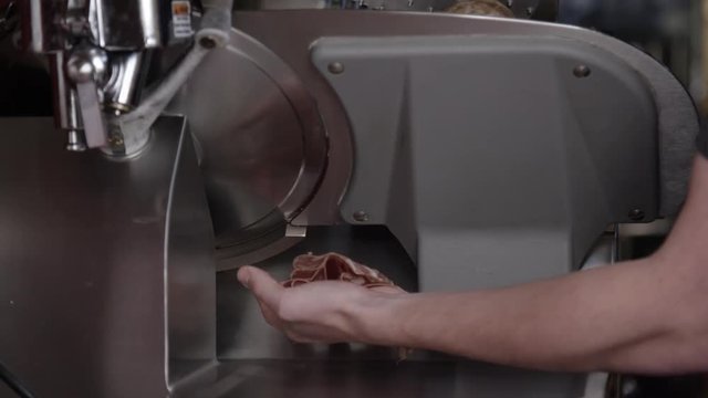 Person catches salami slices from meat cutter, slow motion