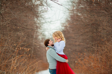 beautiful young couple in love in sweaters walking on snowy forest park