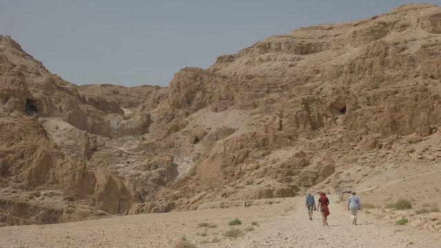 long shot of tourists walking towards the caves and hills at qumran near the dead sea in israel