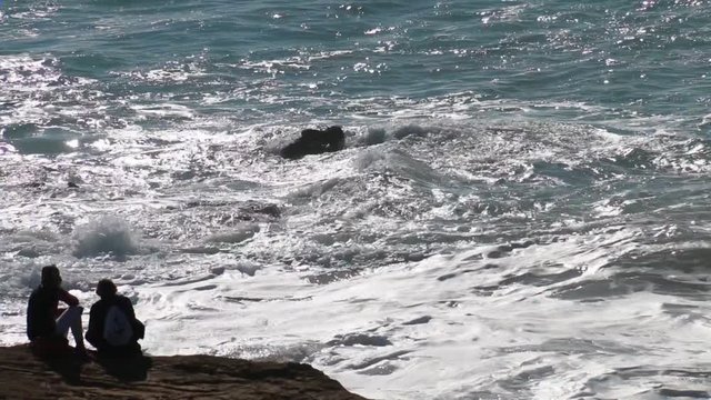 Couple of girls sitting on the edge of a cliff contemplating the strong waves