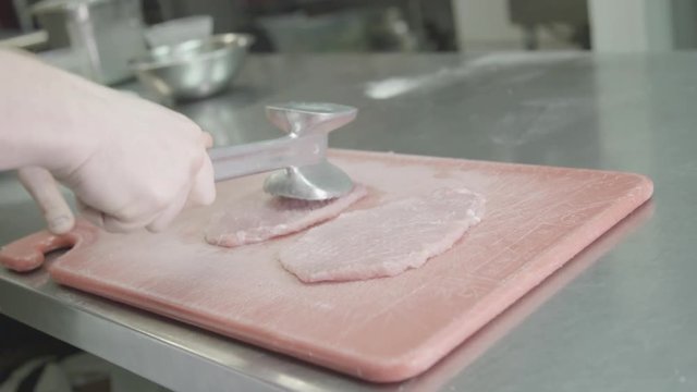 Person tenderizes pork on cutting board, slow motion