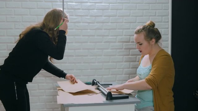 3 shots. Two professional women decorators, designers working with kraft paper and using paper cutter, guillotine at workshop, studio. Crafting work, decoration and art concept