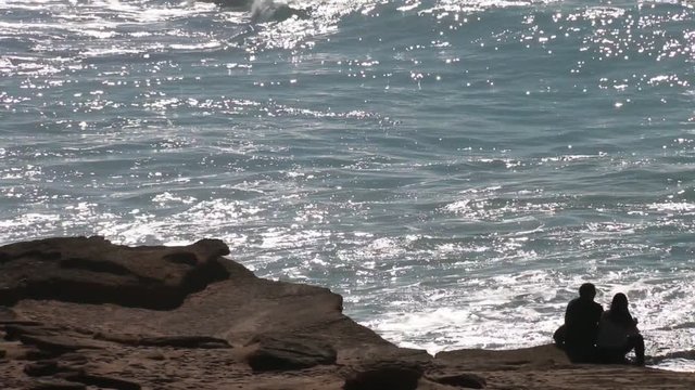 Man and woman couple sitting on the edge of a cliff contemplating the strong waves