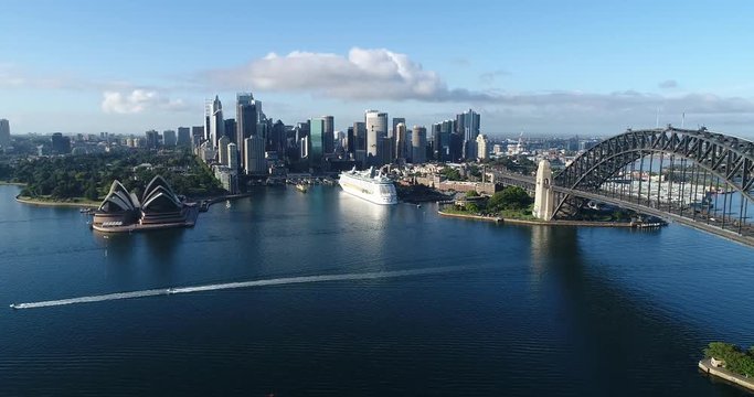 High mid-air forward flying towards Sydney city CBD landmarks over waters of Harbour with Sydney harbour bridge on the right facing Circular Quay.
