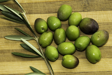 Green olives and leaves  ready to eat in chopping board background.