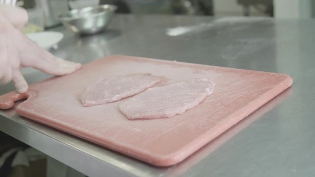 Slow motion, chef tenderizes pork on cutting board