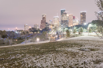 Downtown Houston at twilight with big and fluffy snowflakes fell on meadow grass at Eleanor Tinsley Park. Park lawn, curved bike pathway, modern skylines in background. Snow is extremely rarely here
