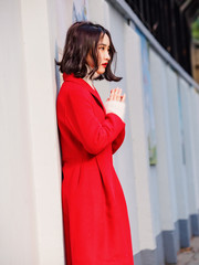 Fototapeta premium Beautiful young brunette woman wearing a red coat in autumn city. Outdoor fashion portrait of glamour young Chinese cheerful stylish lady in street. Emotions, people, beauty and lifestyle concept.
