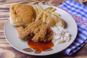 Dinner setting of fried chicken, mashed potatoes with bun and coleslaw on wooden background