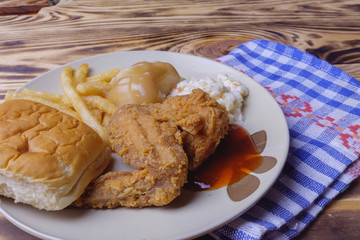 Dinner setting of fried chicken, mashed potatoes with bun and coleslaw on wooden background