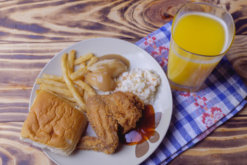 Dinner setting of fried chicken, mashed potatoes with bun and coleslaw on wooden background