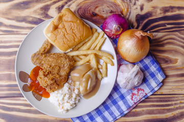 Dinner setting of fried chicken, mashed potatoes with bun and coleslaw on wooden background