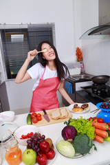 Cheerful woman is covering her eye with spoon in kitchen room