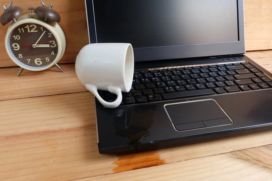 Coffee Cup spill out on Laptop Keyboard on wooden floor, Accident computer repair concept.