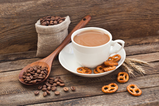 Coffee in a cup with coffee beans and cracker on a wooden background