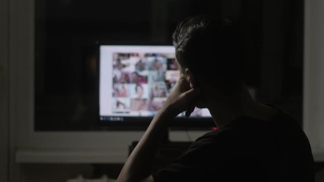 young man watching surfing pornography site on the web at night at home