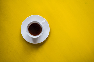 white coffee cup on a white dish with coffee on yellow background
