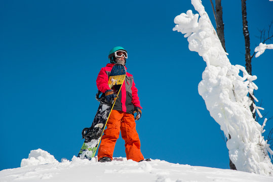 Male snowboarder standing on top of the mountain with his snowboard on a sunny winter day at winter ski resort. Blue sky on the background copyspace lifestyle enjoyment sportsman seasonal concept