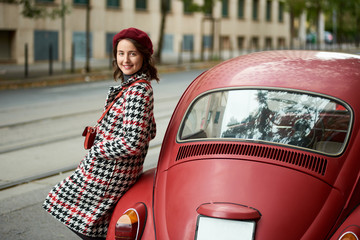 Red retro car behind and a cute girl near it. Close-up. The girl is dressed in a coat and beret with in red tones. Vintage style . Lifestyle concept with autumn on background