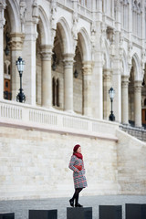 Obraz na płótnie Canvas Woman stands against the backdrop of a powerful European architectural structure. She has a red beret and a handbag, a coat in tone. The concept of the autumn