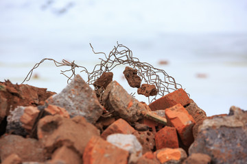 A pile of construction debris with broken bricks and concrete in winter against a background of snow.