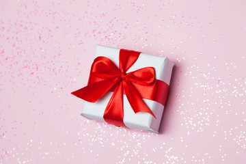 gift box vith red bow and glitter sparkles on pink background. st. Valentine's day concept