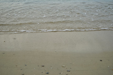 Soft sand and small rock beach with sea water and white foamy wave background and copyspace on Ornos shore