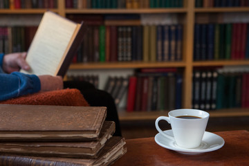 Naklejka premium Sweet moments of relaxation with books and a cup of coffee. Vintage books, glasses, chair, library, man