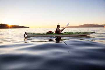 Girl Kayaking during a colorful and vibrant Sunset. Taken near Jericho Beach, Vancouver, British Columbia, Canada.