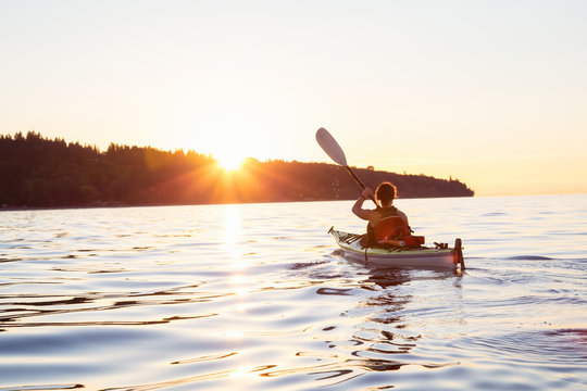Adventure Girl kayaking on a sea kayak during a colorful and vibrant sunset. Taken near Jericho Beach, Vancouver,
