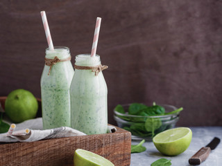 Two spinach smoothies with lime in the glass bottles with straws