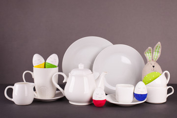 set of white utensils for lunch and tea party and funny easter bunny on a gray background. Easter set for table service