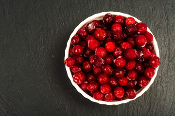 Frozen berries of cranberries in white bowl on black stone