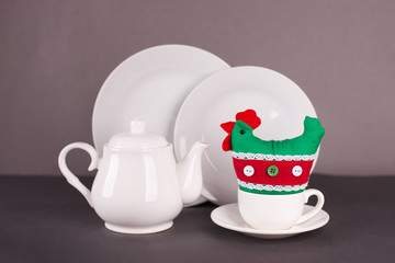 set of white utensils for Easter tea drinking and decorative chicken on a gray background. Spring home concept