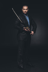 mature man in suit with japanese katana sword on black