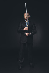man in suit holding japanese katana sword in front of his face on black