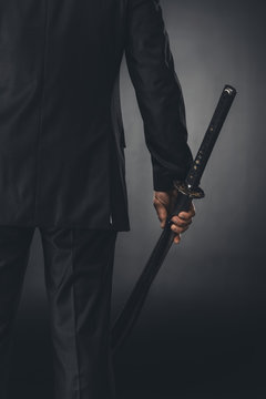 Cropped Shot Of Man In Business Suit With Katana Sword On Black