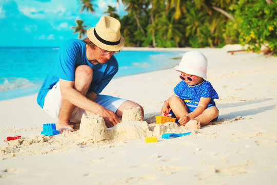 father and little daughter playing with sand on beach