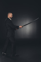 side view of mature man in suit with katana sword on dark background