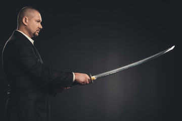 side view of man in suit with katana sword isolated on black