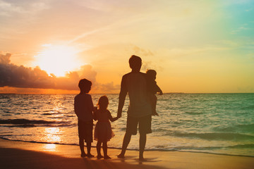 father with three kids walking on beach at sunset