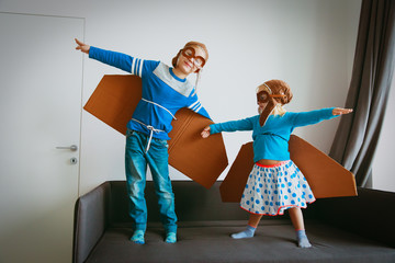 Fototapeta na wymiar little boy and girl with pilot glasses and wings play fly at home