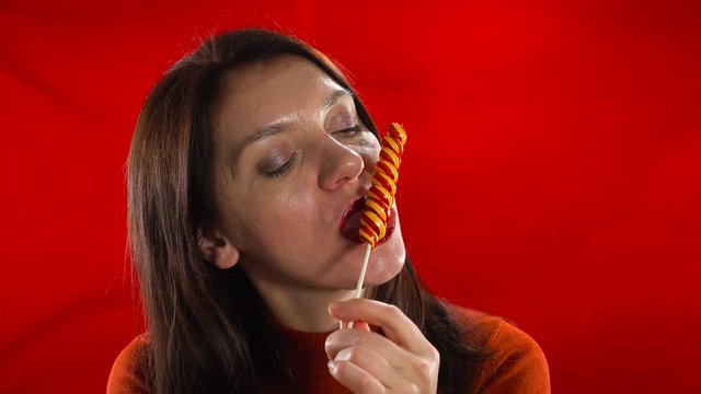 Sensual European model erotic sucks candy. Studio, red background.