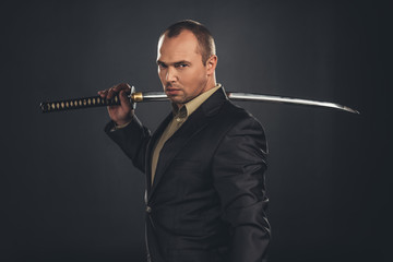 serious man in suit with katana sword isolated on black