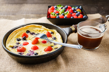 Fresh homemade dutch baby pancake with blueberry raspberry and strawberry in a pan on a table.
