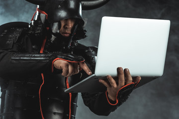 Fototapeta na wymiar close-up shot of samurai using laptop on dark background with smoke