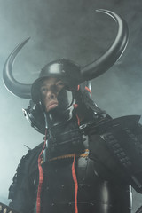 bottom view of samurai in traditional armor on dark background with smoke