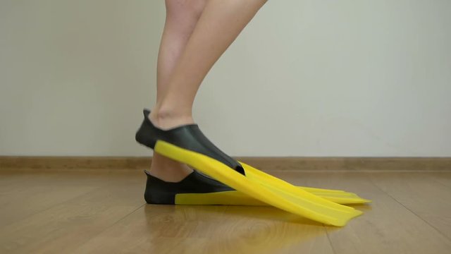 Legs of a woman, shod in flippers for diving, walks the floor in the room