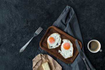 top view of fried eggs, butter and cup of coffee for breakfast on dark tabletop